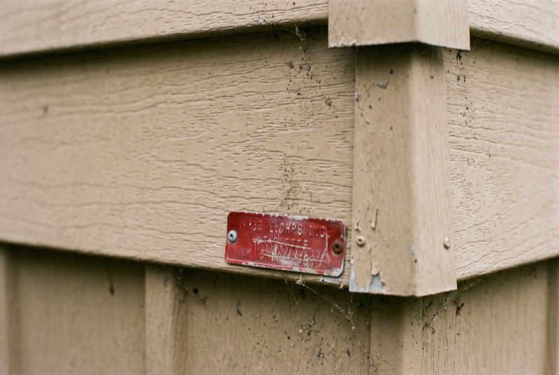 A small red metal certification tag riveted to the siding of a manufactured home